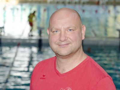 Trainer Ronny Rosenow im roten T-Shirt. Im Hintergrund ein Schwimmbecken.