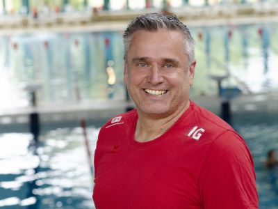 Trainer Ingo Greif im roten T-Shirt. Im Hintergrund ein Schwimmbecken.
