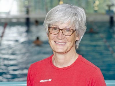 Trainerin Petra Petrov im roten T-Shirt. Im Hintergrund ein Schwimmbecken.