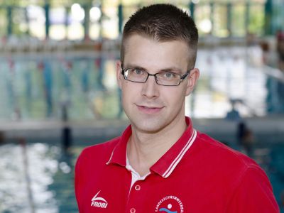Fachwart für Sport Felix Schulz im roten T-Shirt. Im Hintergrund ein Schwimmbecken.