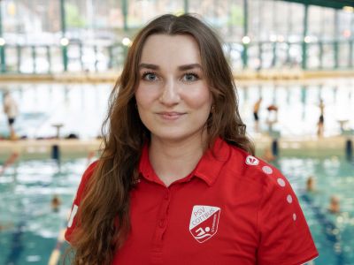 Trainerin Greta Jentsch im roten T-Shirt. Im Hintergrund ein Schwimmbecken.