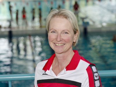 Trainerin Tina Bork im roten T-Shirt. Im Hintergrund ein Schwimmbecken.
