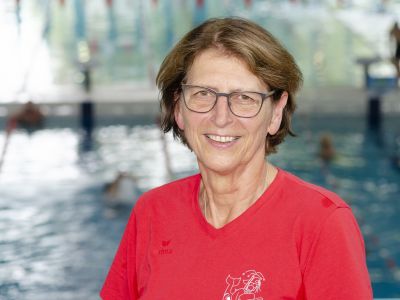 Trainerin Regine Bräuer im roten T-Shirt. Im Hintergrund ein Schwimmbecken.